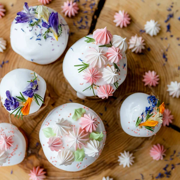 Ortodoks Paskalya 2021. Pasta dekorasyonu. Beyaz kremalı kekler, pembe ve beyaz kremayla süslenmiş, çiçekler ve doğal ahşap arka planda bitkiler. Paskalya kartı.