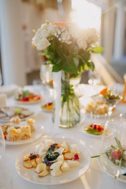 Düğün masasına servis yapıyorum. Restoran işi. Gözlükler, beyaz tabaklar ve yuvarlak bir masada beyaz bir masa örtüsüyle süslenmiş çatal bıçaklar..
