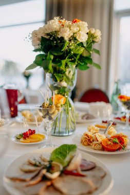 Düğün masasına servis yapıyorum. Restoran işi. Gözlükler, beyaz tabaklar ve yuvarlak bir masada beyaz bir masa örtüsüyle süslenmiş çatal bıçaklar..