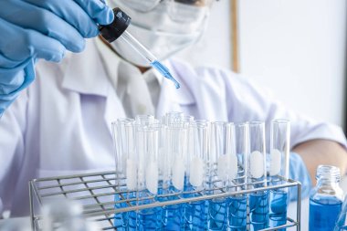 Laboratuvarda virüs ve aşı antiretroviral koronavirüs hakkında çalışan kadın araştırmacı ya da doktor test tüpleri ve mavi sıvı çözeltisi ile araştırma yapıyor..