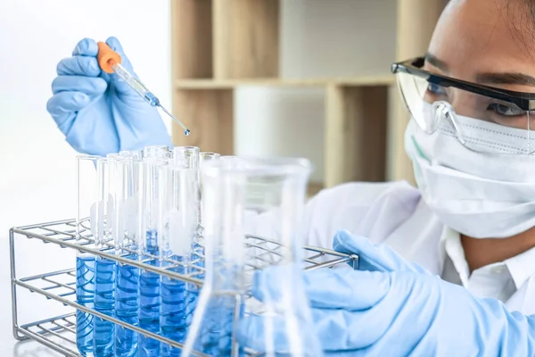 Female scientific researcher or doctor working in laboratory about virus and vaccine antiretroviral coronavirus covid19 researcher investigations with test tubes flask and blue liquid solution.