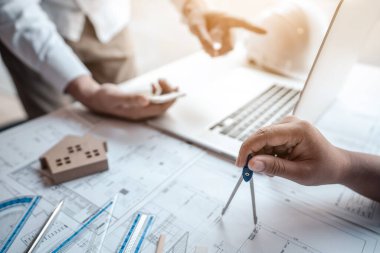 Mimarlar veya mühendislik ekibi, modern ofisteki tasarım ve model ev üzerine yeni mimari projeler planlayan nesneler, araçlar ve inşaat çizimleri üzerinde danışmanlık ve analiz yapıyor..