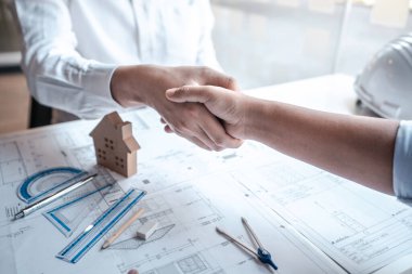 Mimarlar ya da mühendislerden oluşan bir ekip, mühendis araçları ve inşaat çizimleri denetimi üzerinde çalışırken el sıkışırken, mimari proje planlama, model ev hakkında tartışır..