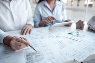 Mimarlar veya mühendislik ekibi, modern ofisteki tasarım ve model ev üzerine yeni mimari projeler planlayan nesneler, araçlar ve inşaat çizimleri üzerinde danışmanlık ve analiz yapıyor..