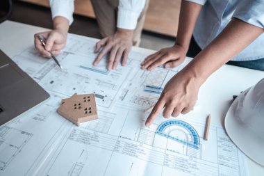 Mimarlar veya mühendislik ekibi, modern ofisteki tasarım ve model ev üzerine yeni mimari projeler planlayan nesneler, araçlar ve inşaat çizimleri üzerinde danışmanlık ve analiz yapıyor..