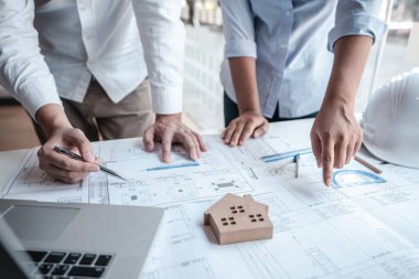 Mimarlar veya mühendislik ekibi, modern ofisteki tasarım ve model ev üzerine yeni mimari projeler planlayan nesneler, araçlar ve inşaat çizimleri üzerinde danışmanlık ve analiz yapıyor..