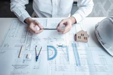 Nesneler üzerinde çalışan mimarlar veya mühendisler araç gereçler ve modern ofisteki plan ve model ev üzerine yeni mimari projeler planlıyorlar..