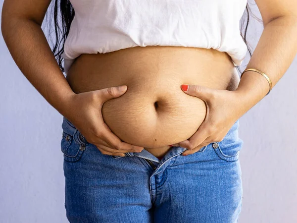 fat belly of an indian woman in jeans held with both hands on white background