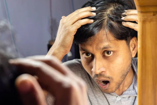 a middle aged Indian man is looking at his hair fall with surprised face in mirror