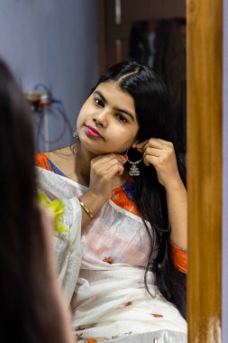 Beyaz sarılı güzel bir Hintli kadın aynanın önünde gülen yüzlü gümüş küpeler takıyor.