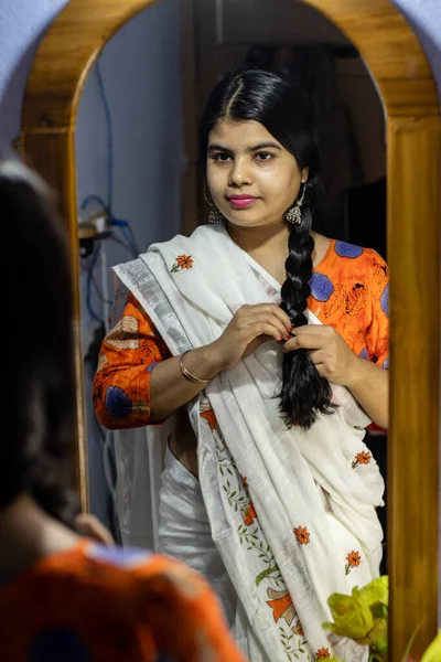 a beautiful Indian woman in white saree knotting hair in front of mirror with smiling face