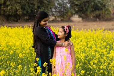 Güzel bir Hintli anne ve kız birbirlerine bakıyorlar ve sarı hardal çiçek tarlasında duruyorlar.