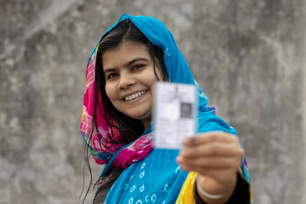 an Indian village woman with smiling face showing blurred voter card in hand