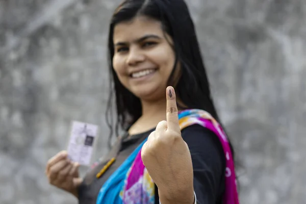 selective focus on ink-marked finger of an Indian woman with smiling face and voter card on other hand