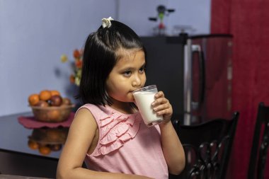 Cam bardaktan süt içen şirin bir Hintli / Asyalı kızın yüz ifadesi. Sağlıklı beslenme kavramı.