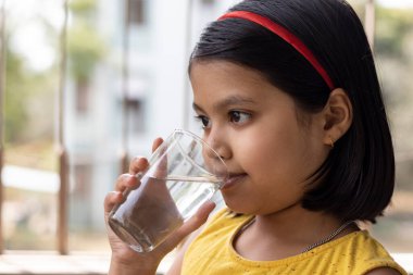 Sarı elbiseli Hintli bir kız çocuğu bardaktan su içiyor.