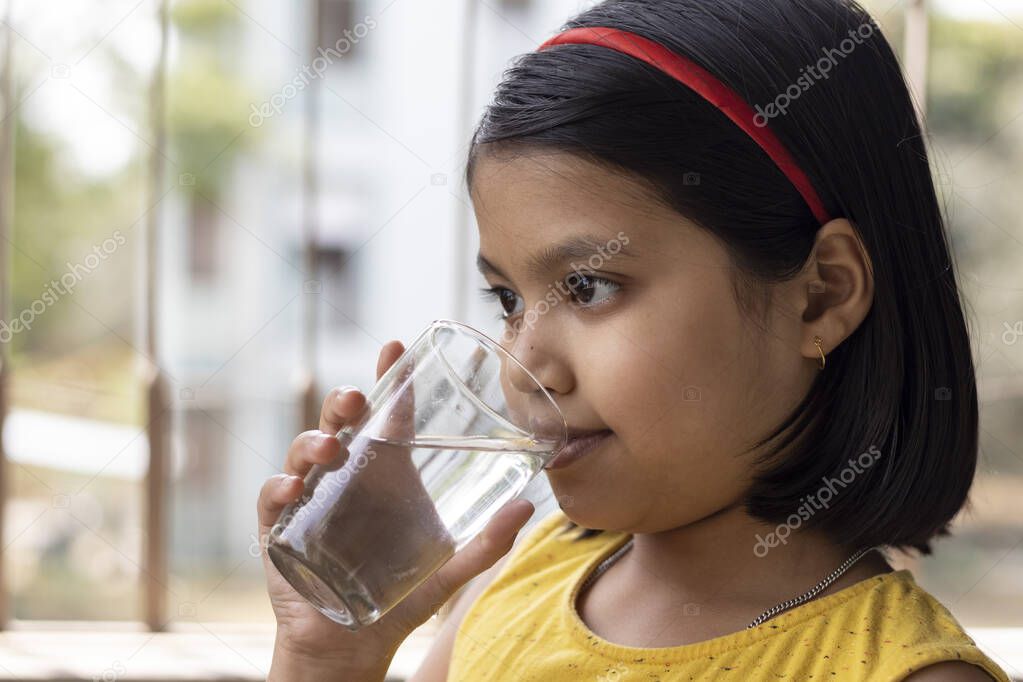 an Indian asian girl child in yellow dress drinking water from a glass