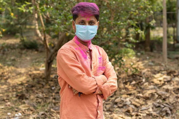 An Indian Bengali man in surgical nose mask and colorful face with powder paint during Holi in pandemic