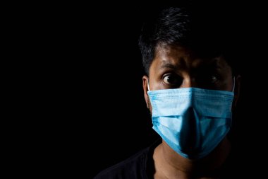 Hintli bir Asyalı erkek cerrahi burun maskesi ve siyah arka planda gözleri açık.