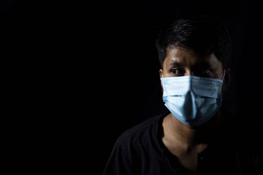 Hint asıllı, burun maskesi takmış, siyah arka plana bakan Asyalı bir erkek.