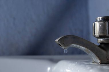 Metal bir lavabo musluğunun yan görünüşü, evdeki odada su damlaları.