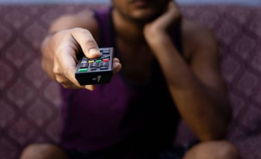 Sıradan giyinmiş, uzaktan kumandayı gösteren Hintli bir Asyalı 'ya odaklan.