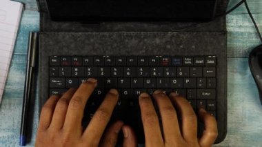 Mini bilgisayar klavyesiyle yazı yazan Hintli bir adamın üst görüntüsü.