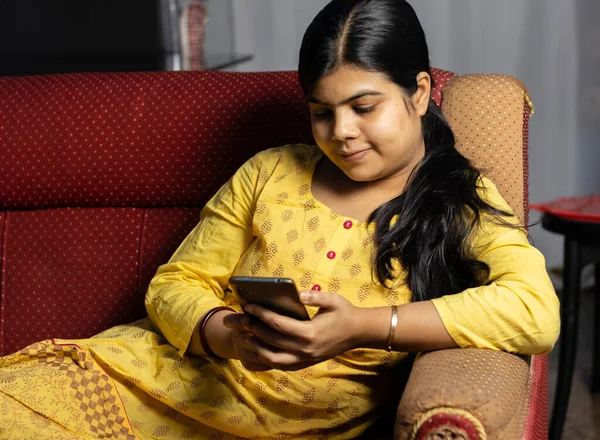 Selective focus of an Indian Asian pretty woman using smart phone sitting on sofa