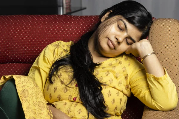 An middle aged Indian woman in yellow dress taking nap on sofa