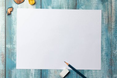 Mavi ahşap zemin üzerine boş beyaz sayfa üst görünüm kalem, silgi, keskinleştirici ile