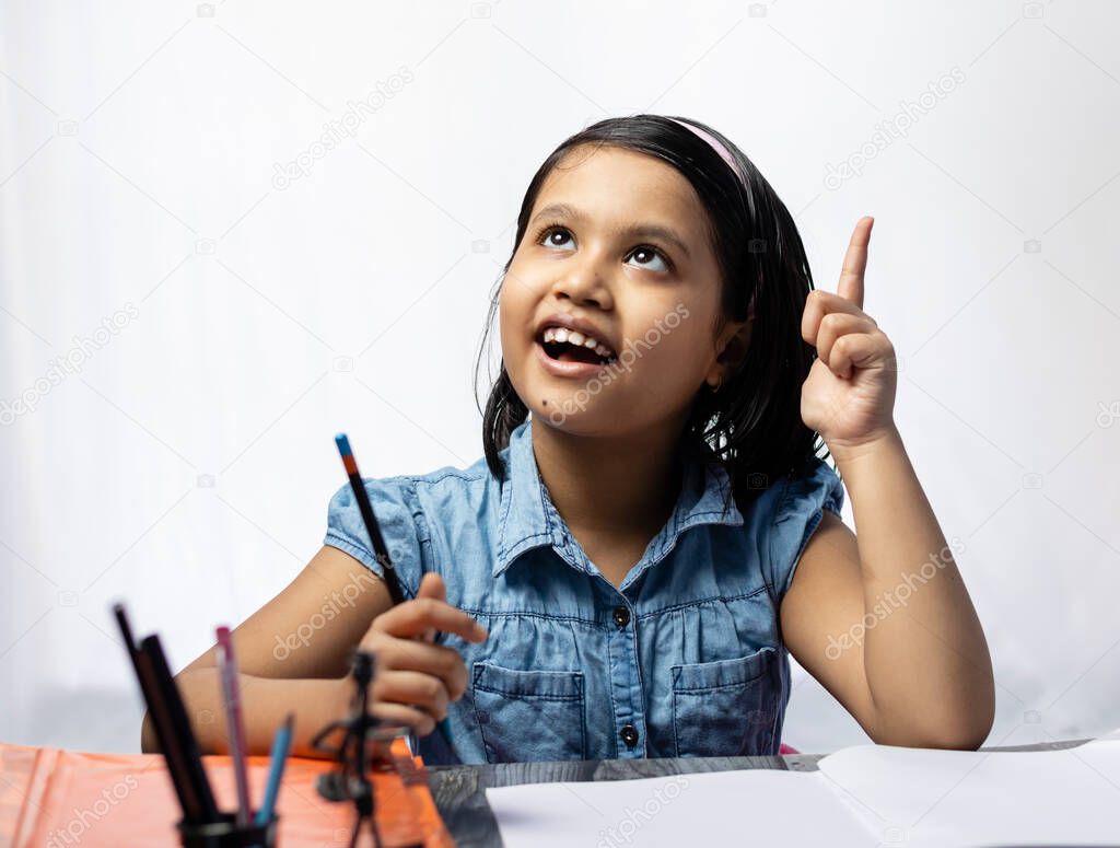 A pretty Indian girl child thinking and looking upward while studying