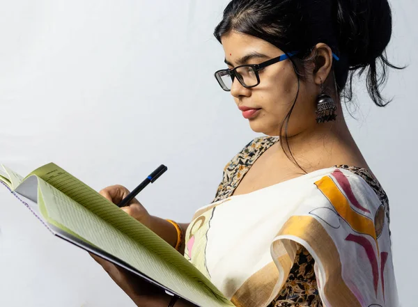 Isolated on white background an Indian office woman in saree writing on notebook with pen side facing