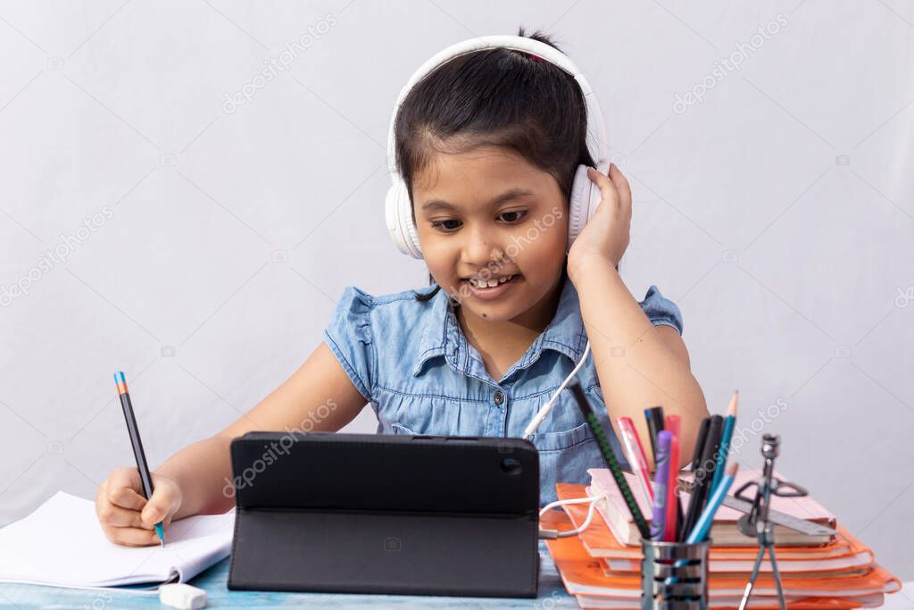 A pretty Indian girl child attending online class with tablet and headphone on white background