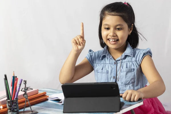 Beyaz arka planda tabletle online derse katılan güzel bir Hintli kız çocuğu.