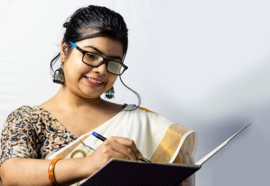 Beyaz arka planda, sari giymiş Hintli bir ofis kadını kalemle deftere yazı yazıyor.