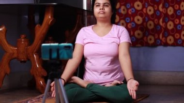 Orta yaşlı Hintli ev hanımı bir kadın fitness yogası ya da meditasyon yapıyor. Akıllı telefon, fitness konsepti önünde.