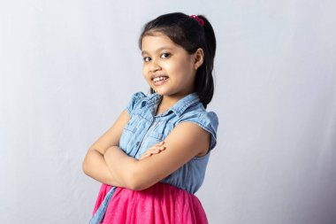 Kolları kapalı gülümseyen sevimli bir Hintli kız çocuğu beyaz arka planda izole edilmiş.