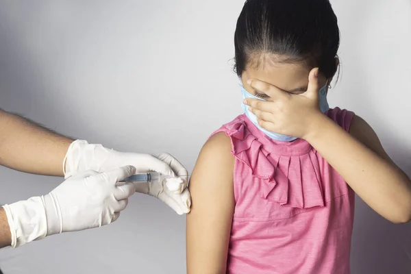An Indian girl child in nose mask receiving vaccine dose covering her eyes on white background