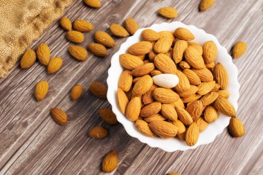 Tahta arka planda beyaz bir kâsede badem fıstığı manzarası.