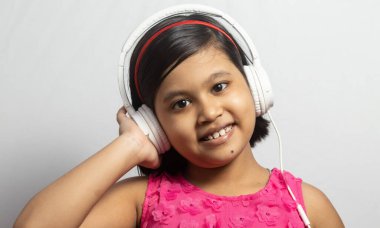 Beyaz arka planda beyaz kulaklığa dokunup müzik dinleyen şirin bir Hintli kız çocuğu.