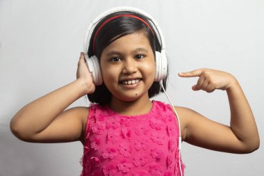 Müzik dinleyen ve beyaz arka planda beyaz kulaklığı olan şirin bir Hintli kız çocuğu.