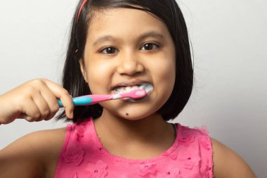 Beyaz arka planda diş fırçasıyla dişlerini fırçalayan Hintli bir kızın vesikalık fotoğrafı.