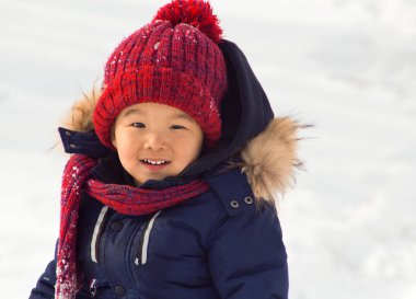 Küçük Asyalı çocuk kış kıyafetleriyle karda oynuyor. Kazak çocuk..