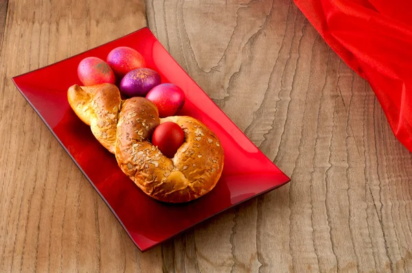 木製の背景に色の卵を持つ光沢のある赤いプレート上にギリシャの伝統的なイースターパン Tsourec と呼ばれる — ストック写真