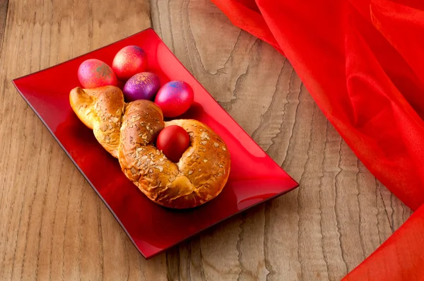 木製の背景に色の卵を持つ光沢のある赤いプレート上にギリシャの伝統的なイースターパン Tsourec と呼ばれる — ストック写真