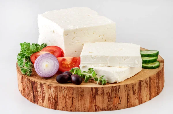Bitki ve sebzelerle süslenmiş doğal ahşap tabakta Feta peyniri..