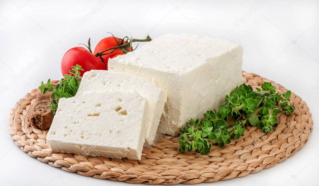 Feta cheese on a nice wicker plate decorated with herbs and veggies