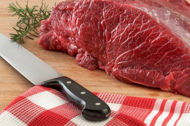 Tahtada, üzerinde bıçak ve masa örtüsü olan çiğ et yığını..