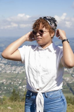 Güneş gözlüklü, kıvırcık sarı saçlı ve kafasında eşarp olan İspanyol bir kadının vücut görüntüsünün yarısı Dominik Cumhuriyeti 'nin kırsal kesiminde güneşli bir tatil gününde duruyor.