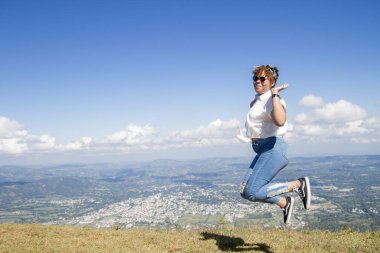 Çekici bir Latin Amerikalı genç bayan güneş gözlüklü mutlu ve atlıyor uzak Dominik şehri manzaralı bir yaz günü gezisine